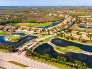 Aerial view of a gated residential community in Naples, Florida, featuring landscaped ponds, palm-lined roads, and upscale homes surrounded by greenery.